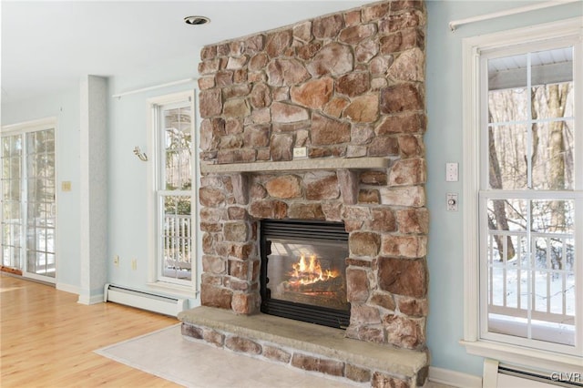 details with baseboards, a stone fireplace, baseboard heating, and wood finished floors