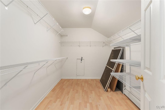 walk in closet with lofted ceiling, a baseboard radiator, and wood finished floors