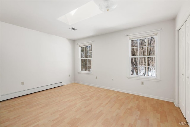 spare room with a baseboard radiator, a skylight, visible vents, a wealth of natural light, and light wood finished floors