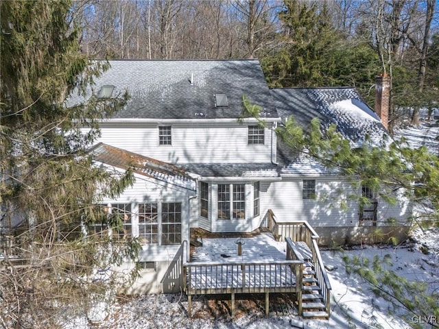 snow covered house featuring a deck, a shingled roof, and a chimney