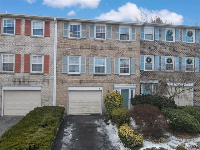 multi unit property with driveway, a garage, and brick siding