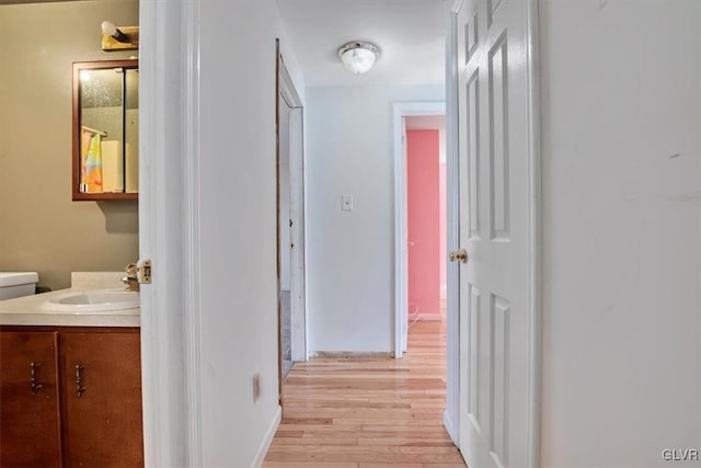 hall with a sink, light wood-style flooring, and baseboards