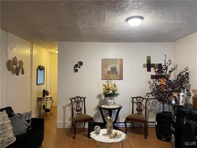 sitting room featuring baseboard heating, a textured ceiling, baseboards, and wood finished floors