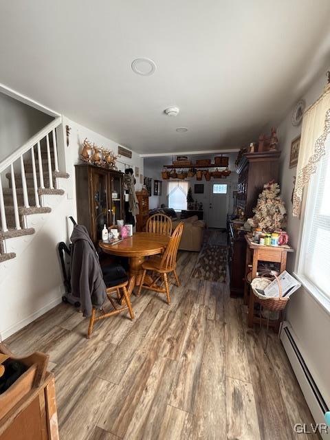 dining space with a baseboard heating unit, stairway, and wood finished floors