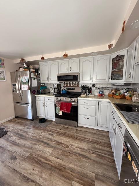 kitchen with tasteful backsplash, white cabinets, appliances with stainless steel finishes, dark wood-style flooring, and light countertops