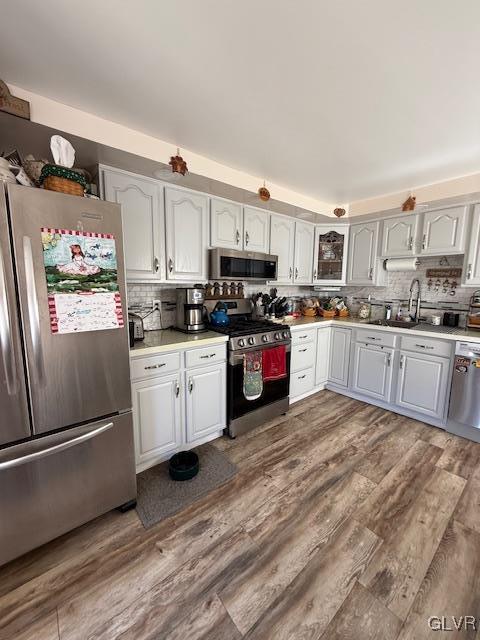 kitchen with stainless steel appliances, light countertops, decorative backsplash, white cabinets, and wood finished floors