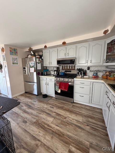 kitchen with stainless steel appliances, dark wood-style flooring, white cabinetry, light countertops, and decorative backsplash