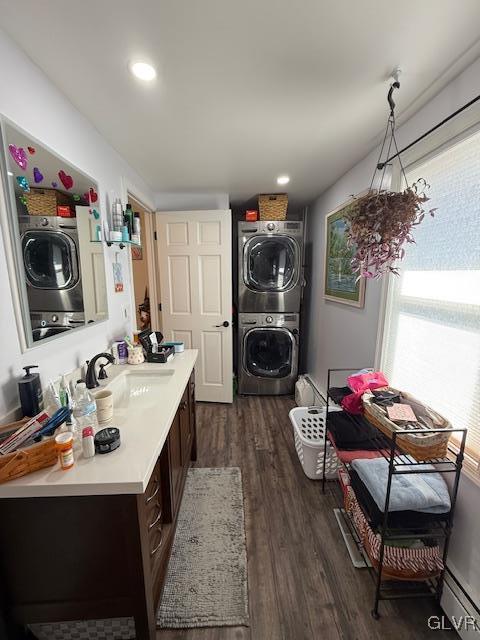 clothes washing area featuring dark wood-style flooring, stacked washer and dryer, baseboard heating, a sink, and laundry area