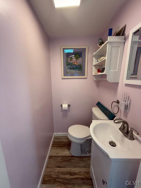 half bathroom featuring baseboards, vanity, toilet, and wood finished floors