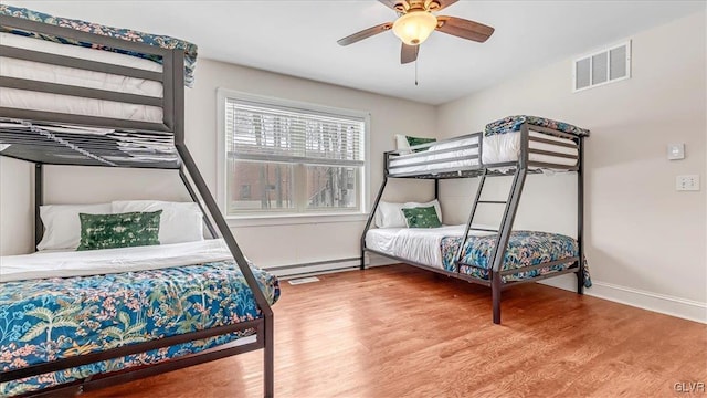 bedroom with baseboards, visible vents, baseboard heating, and wood finished floors