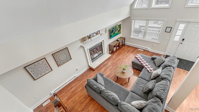 living room featuring a baseboard radiator, visible vents, wood finished floors, and a glass covered fireplace