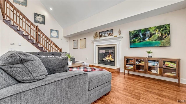 living area featuring baseboards, a glass covered fireplace, wood finished floors, stairs, and baseboard heating