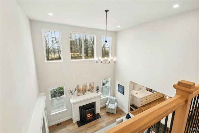 interior space with a warm lit fireplace, recessed lighting, baseboards, light wood-style floors, and an inviting chandelier