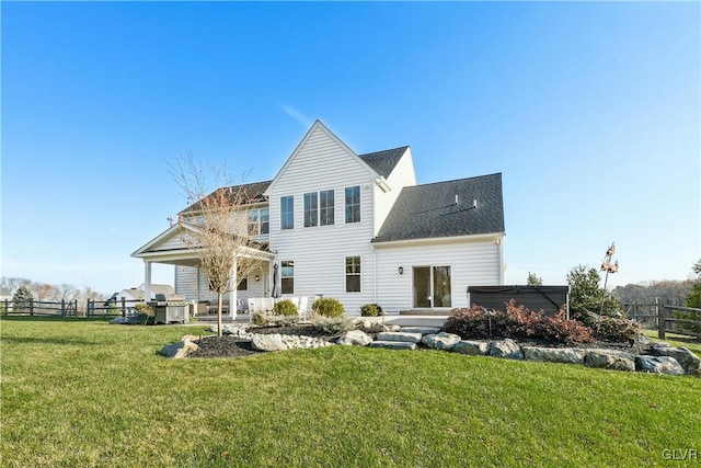 rear view of house with a lawn, fence, and a hot tub