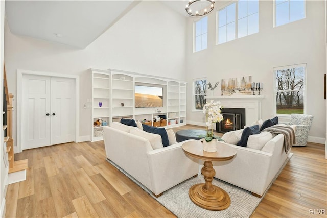 living room with a warm lit fireplace, high vaulted ceiling, a chandelier, baseboards, and light wood-style floors