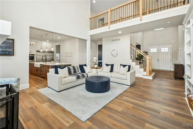 living area with a high ceiling, stairway, wood finished floors, and visible vents