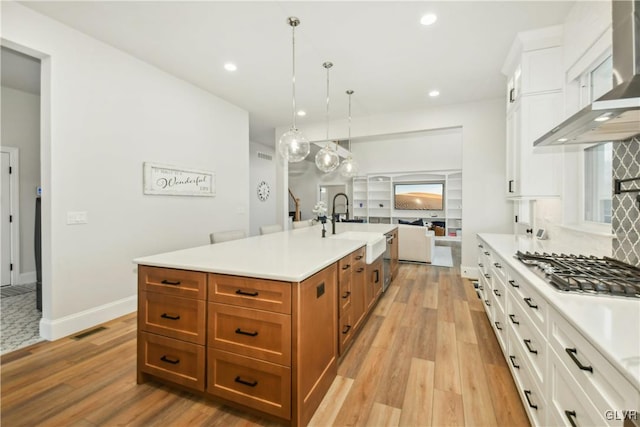 kitchen with open floor plan, light countertops, wall chimney range hood, pendant lighting, and a sink