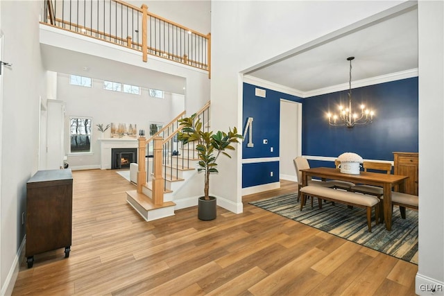 dining space featuring a fireplace with flush hearth, ornamental molding, stairway, light wood-type flooring, and an inviting chandelier