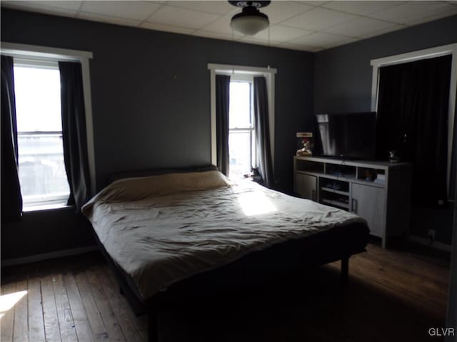 bedroom featuring dark wood-style flooring, a drop ceiling, and baseboards