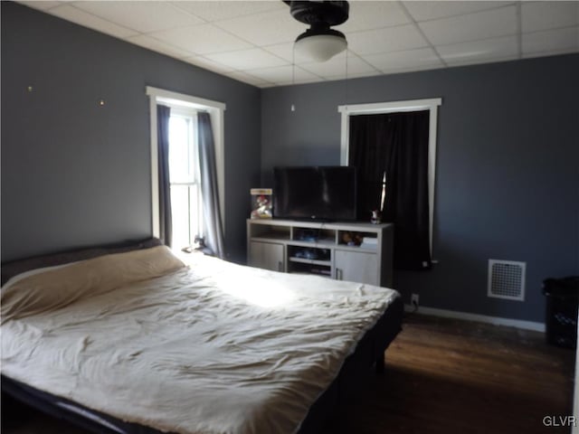 bedroom with ceiling fan, a drop ceiling, dark wood-style flooring, visible vents, and baseboards