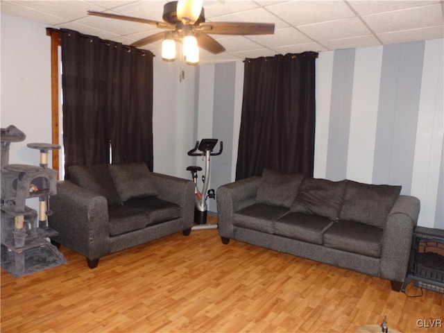 living area featuring a drop ceiling, ceiling fan, and light wood finished floors