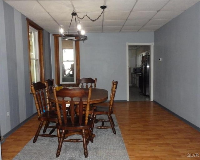 dining room featuring a drop ceiling, wood finished floors, and an inviting chandelier