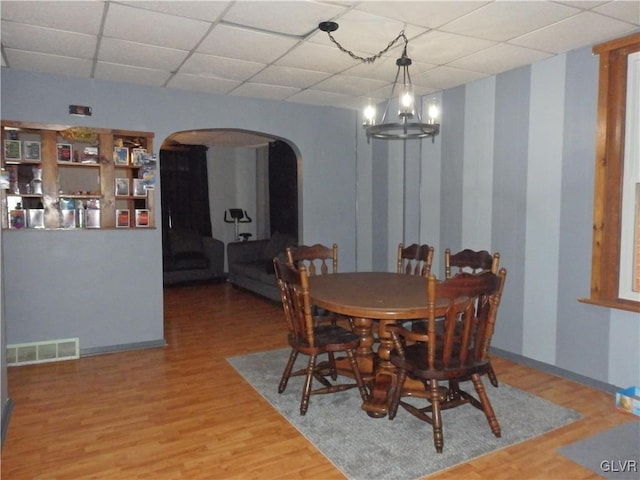 dining room featuring light wood-style floors, visible vents, arched walkways, and a drop ceiling