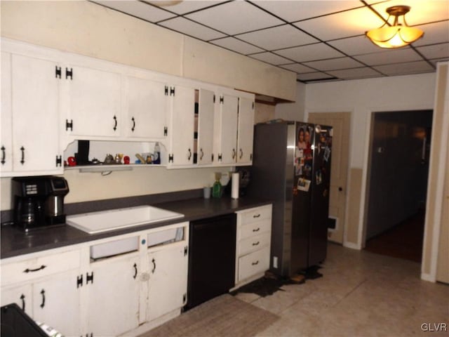 kitchen with a drop ceiling, white cabinetry, black dishwasher, freestanding refrigerator, and dark countertops