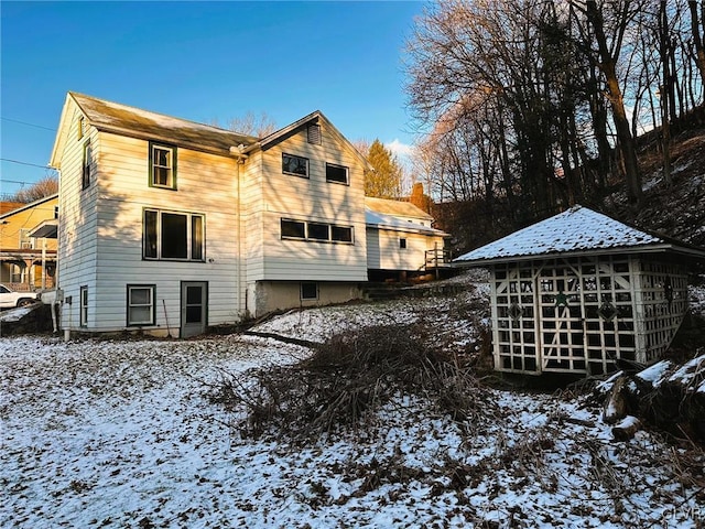 snow covered back of property with a sunroom