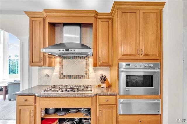 kitchen featuring decorative backsplash, light stone counters, appliances with stainless steel finishes, wall chimney range hood, and a warming drawer