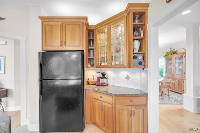 kitchen with glass insert cabinets, light stone counters, freestanding refrigerator, light wood-style floors, and backsplash