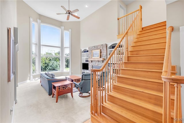 staircase featuring ceiling fan, a high ceiling, baseboards, and carpet flooring