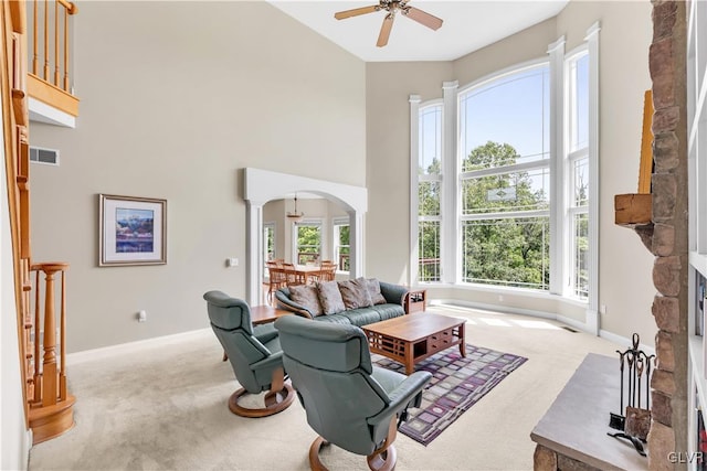 living room with arched walkways, light colored carpet, a fireplace, a towering ceiling, and visible vents