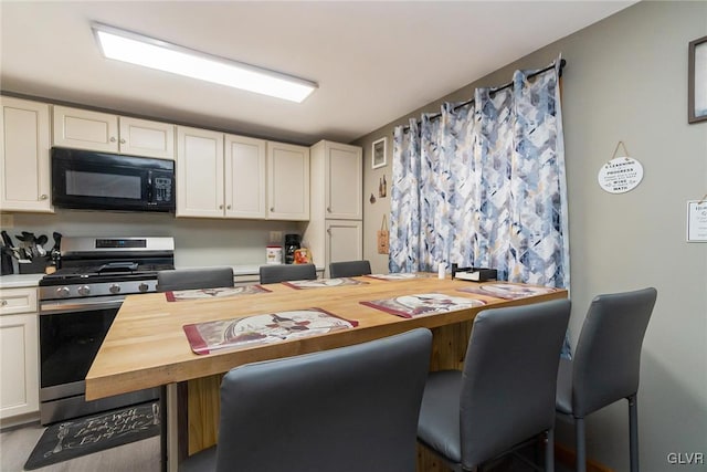 kitchen with black microwave, stainless steel gas range oven, wood counters, and white cabinets