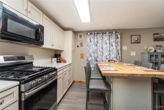 kitchen with a breakfast bar area, wooden counters, white cabinets, gas range, and black microwave