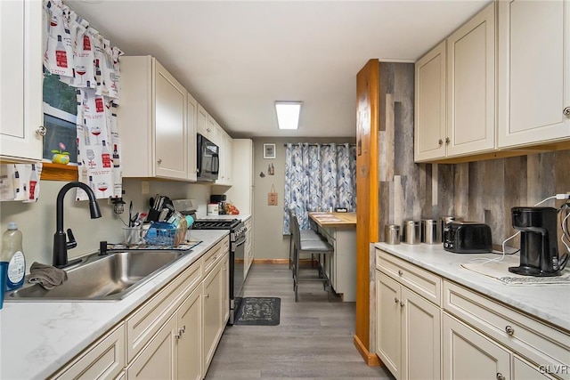 kitchen featuring stainless steel gas stove, a sink, wood finished floors, black microwave, and baseboards