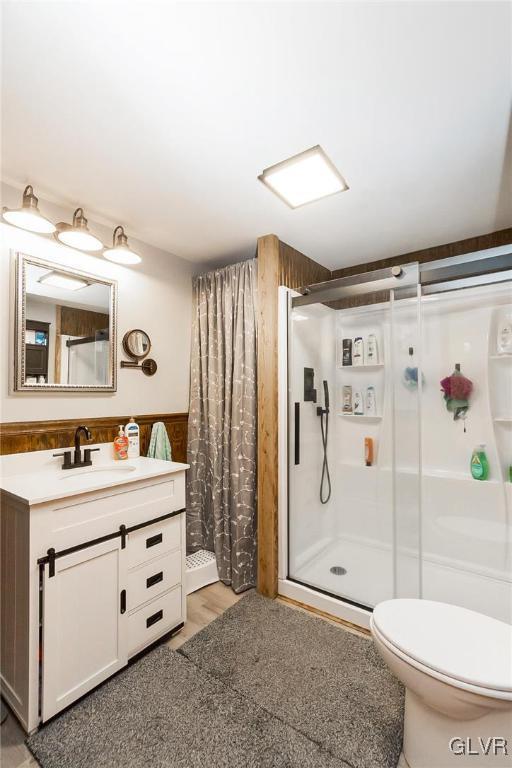 bathroom featuring toilet, a stall shower, wainscoting, and vanity