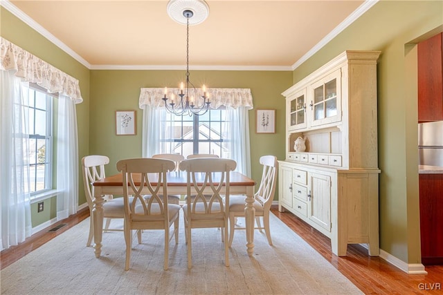 dining room featuring plenty of natural light, ornamental molding, light wood-type flooring, and an inviting chandelier