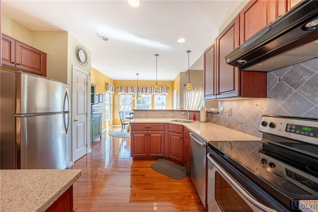 kitchen featuring under cabinet range hood, a peninsula, appliances with stainless steel finishes, backsplash, and pendant lighting