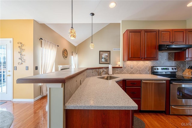 kitchen with under cabinet range hood, a sink, appliances with stainless steel finishes, light wood finished floors, and decorative light fixtures