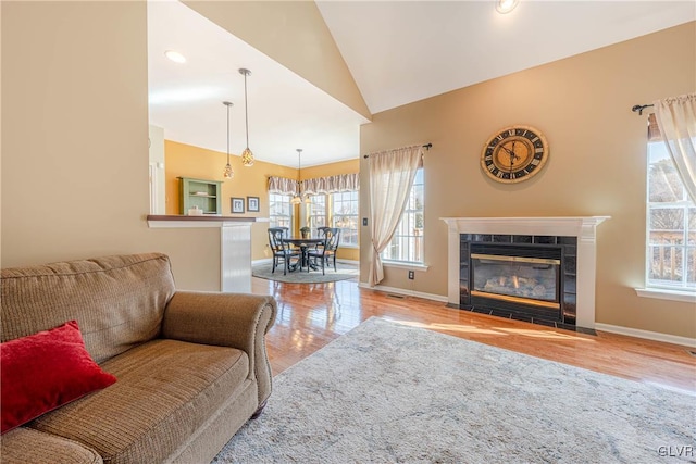 living area with lofted ceiling, light wood finished floors, a tile fireplace, and baseboards