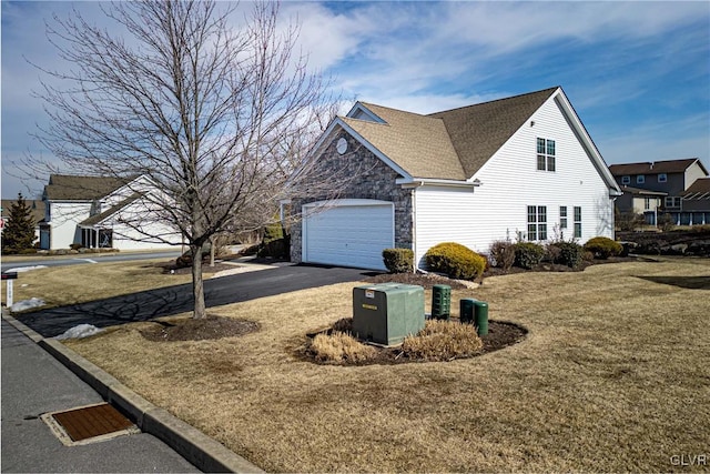 view of side of home featuring stone siding, aphalt driveway, roof with shingles, an attached garage, and a yard