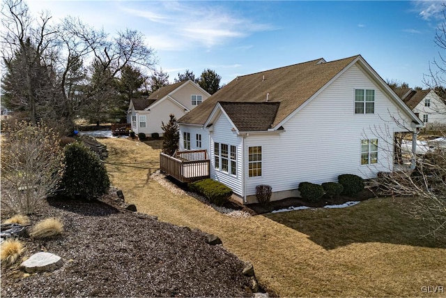 rear view of property with a shingled roof, a lawn, and a deck