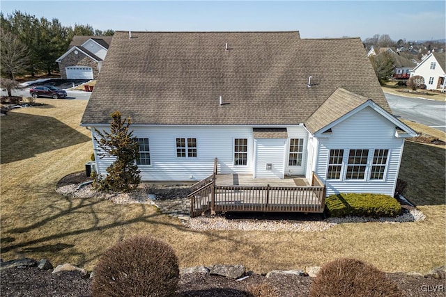 rear view of property with roof with shingles, a lawn, and a wooden deck