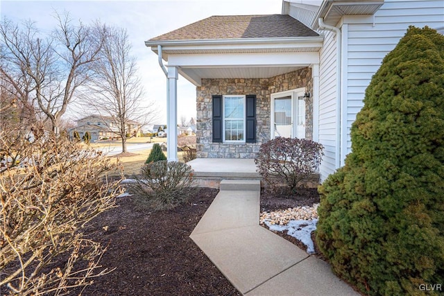 doorway to property with stone siding, a porch, and a shingled roof