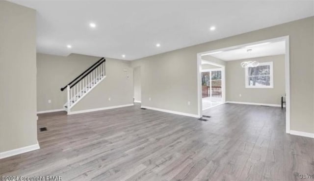 unfurnished living room featuring recessed lighting, wood finished floors, baseboards, stairs, and an inviting chandelier