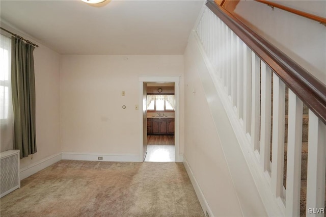 spare room featuring radiator heating unit, baseboards, and light colored carpet