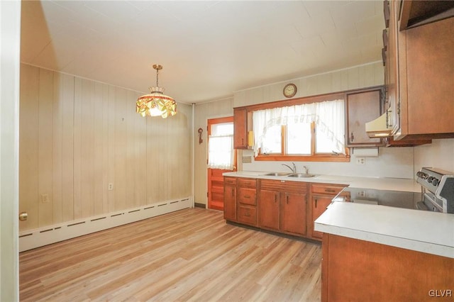 kitchen with brown cabinetry, light countertops, light wood-type flooring, a baseboard heating unit, and a sink