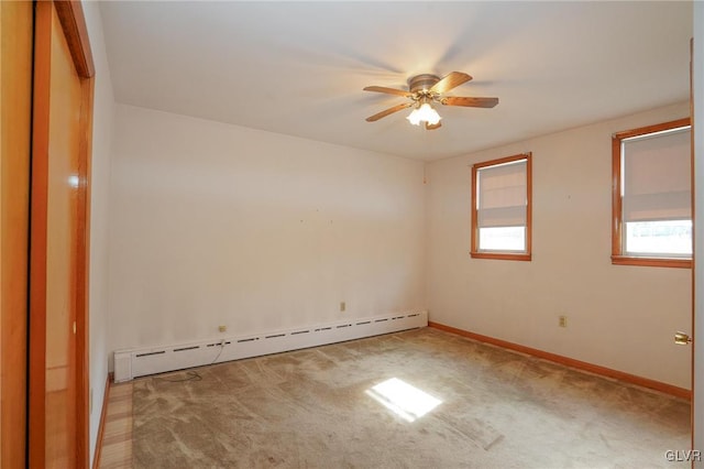 spare room featuring a baseboard heating unit, light colored carpet, baseboards, and a ceiling fan