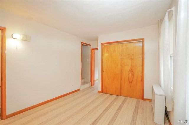 unfurnished bedroom featuring light wood-type flooring, radiator heating unit, baseboards, and a closet